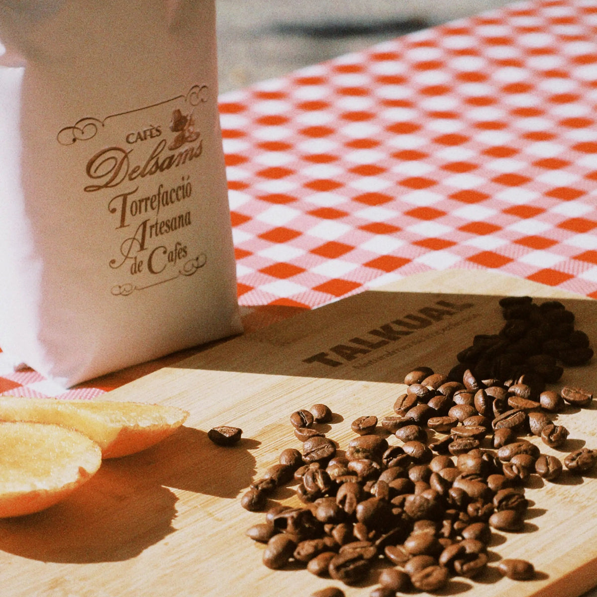 Café en grano Delsams y fruta sobre bandeja de madera TALKUAL