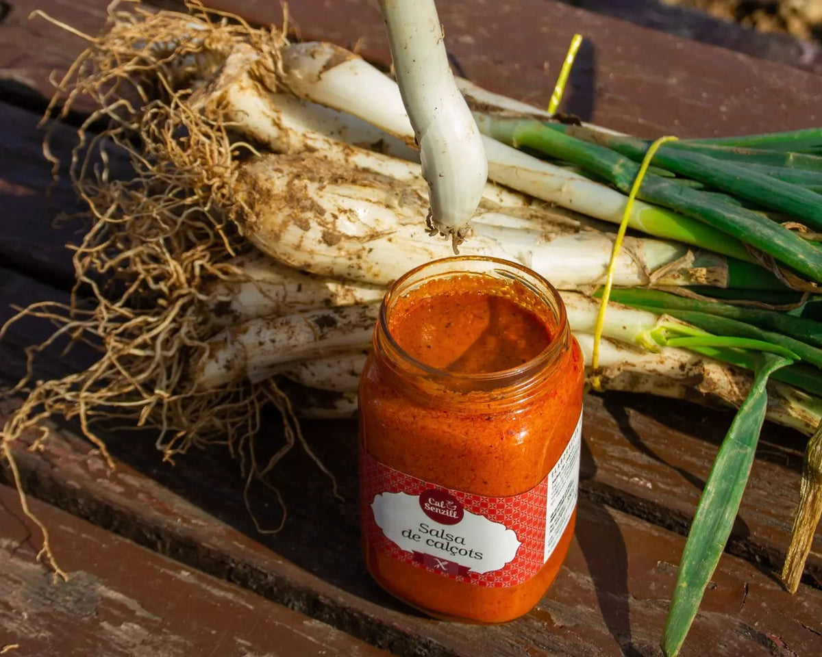 Calçots frescos de temporada amb un pot de salsa romesco en una taula de fusta exterior